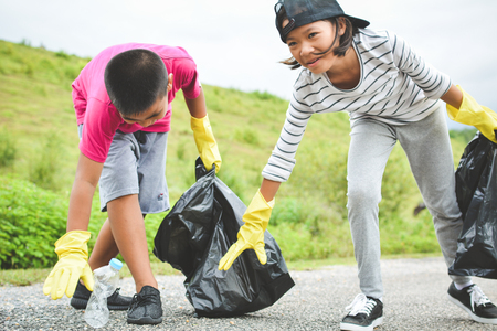 Children hand in yellow gloves picking up empty of bottle plastic into bin bag ,volunteer conceptの写真素材