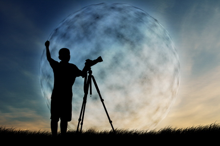 Silhouette of boy using camera shooting moonの写真素材