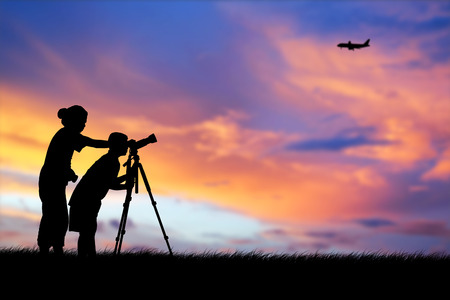 Silhouette of mother and son using camera shooting airplane during the sky sunset backgroundの写真素材
