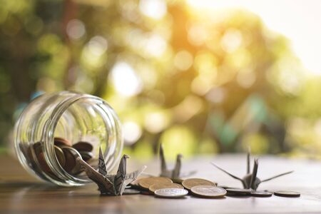 Close up dollar bird and coins in glass jar on wood table, color vintage style ,selective and soft focusの写真素材