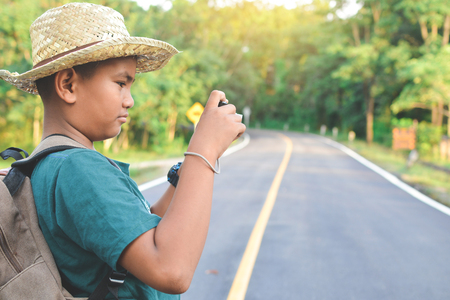 Happy Asian boy backpack in the road and forest background, Relax time on holiday concept travel ,color of vintage tone and soft focusの写真素材