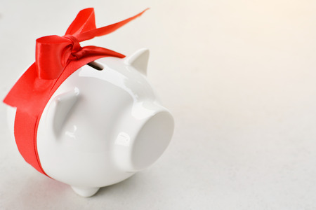 Piggy bank with red ribbon tape on whiteの写真素材