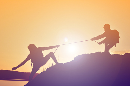 Silhouette of girl helping man teamwork success on top mountain during sky sunsetの写真素材