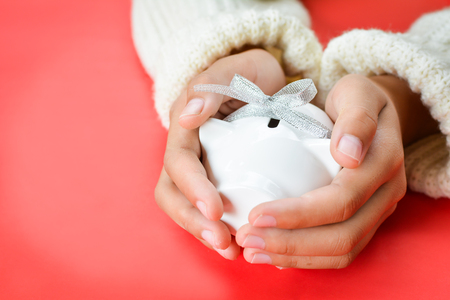 Hand of girl holding white piggy bank and ribbon type on red background with copy space ,concept save moneyの写真素材