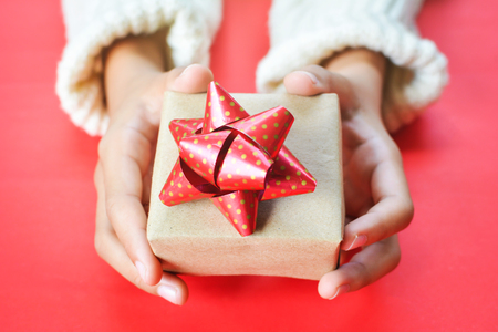 Hands of girl holding gift box on red background for Christmas conceptの写真素材