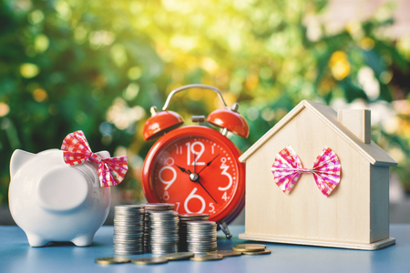 White piggy bank and alarm clock with wood house on table tree bokeh background ,concept save money ,selective and soft focusの写真素材