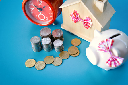 White piggy bank and alarm clock with wood house on table,concept save money ,selective and soft focusの写真素材