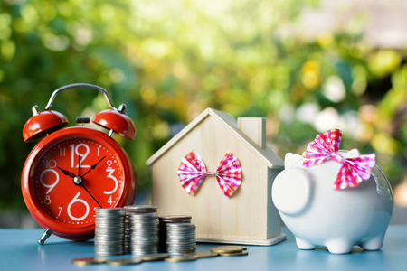 White piggy bank and alarm clock with wood house on table tree bokeh background ,concept save money ,selective and soft focusの写真素材