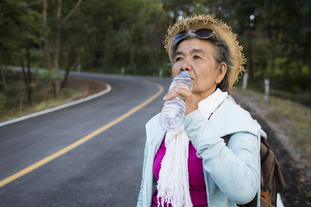 Happy hipster old women drinking water of bottle during backpack traveling on the road relax time in holiday, color vintage style selective and soft focusの写真素材