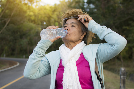 Happy hipster old women drinking water of bottle during backpack traveling on the road relax time in holiday, color vintage style selective and soft focusの写真素材