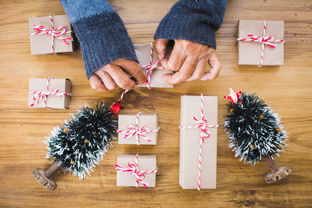 Old female hand holding paper gift box with pine tree  on brown wood background, Merry Christmas and Happy New year concept,selective and soft focusの写真素材