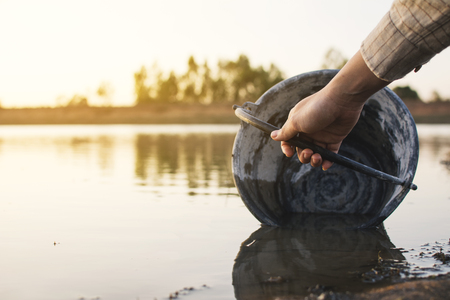 Close-up hand of woman holding a bucket on lake, crisis of water and droughtの写真素材