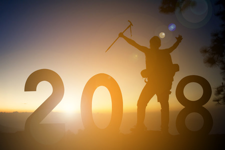 Silhouette of man hiking with 2018 word on top mountain trees forest concept happy new year during sunset, winter seasonの写真素材