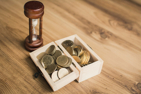 Hourglass with coins on wood table concept time to saving, color of vintage tone