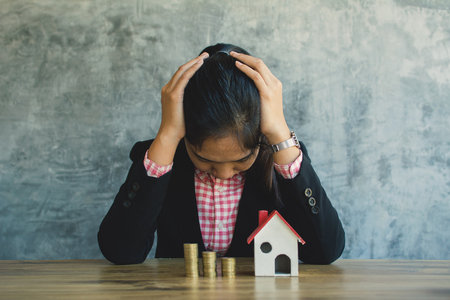 Anxiety businesswoman with model house and coins on desk concept saving and protect  housingの写真素材