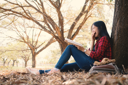 Enjoying moment hipster woman reading a book and sitting under the big tree on park ,Relax time on holiday color of vintage tone and soft focusの写真素材