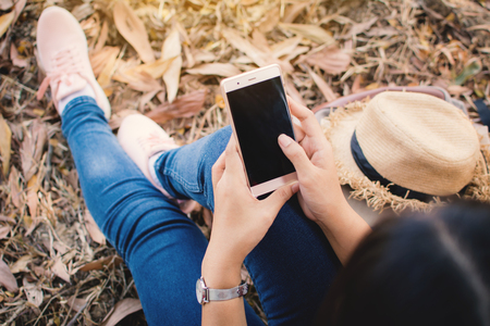 Enjoying moment woman using smartphone sitting under the big tree on park ,Relax time on holiday concept ,color of vintageの写真素材