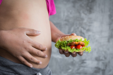 Close up stomach of fat boy enjoy eating with hamburger, concept healthy and lose weight, selective and soft focusの写真素材