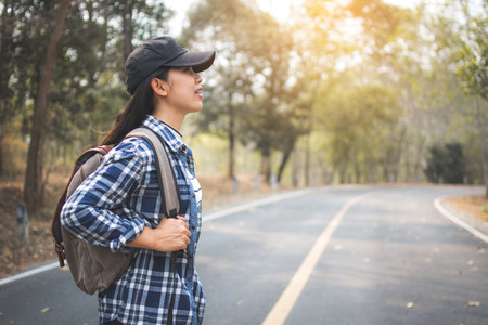 Happy Asian woman backpack in the road and forest background. Relax time on holiday concept travel, color of vintage tone and soft focusの写真素材