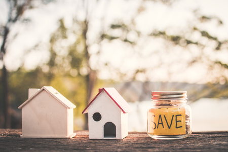 Coins on glass jar with save word and model house on table in nature bokeh background , color vintage style selective and soft focusの写真素材