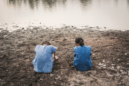 Sad boy and girl sitting on cracked dry ground, Concept drought and shortage of water crisisの写真素材