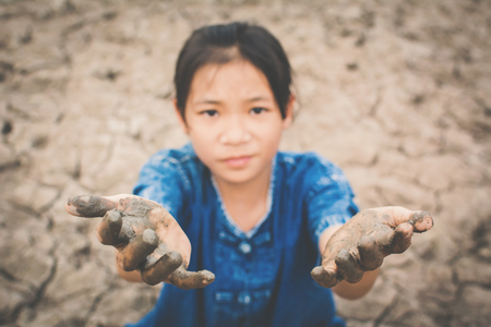 Sad girl praying for the rain on cracked dry ground , Concept drought and shortage of water crisis, selective and soft focusの写真素材