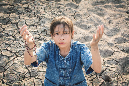 Sad girl praying for the rain on cracked dry ground , Concept drought and shortage of water crisis, selective and soft focusの写真素材