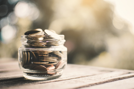Coins on glass jar on table in nature bokeh background , color vintage style selective and soft focusの写真素材