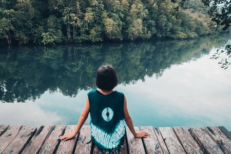Cute girl sitting on the wood plank resting and looking on the river.の写真素材