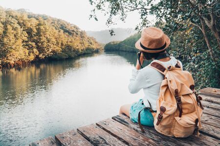 Cute girl backpacking and sitting on the wood plank resting and looking on the river.の写真素材