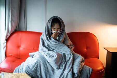 Asian woman have a cold, uses a tissue to cover her mouth when coughing and sneezing at the home, preventing the spread of virus covid 19 ,healthcare concept. selective and soft focus.の写真素材