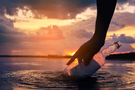 silhouette of hand keeping plastic garbage on the river , save the world and environment.の写真素材