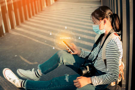 The new normal a girl wearing a mask during travel and public place using smartphone with icon distance.の写真素材