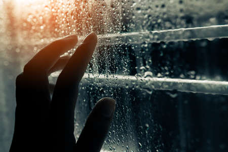female hand touching water droplets on the window in the rainy season.の写真素材