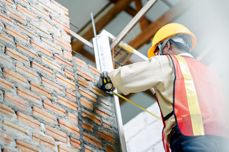 An engineer holding a tape measure inspects the building construction standards to ensure that every...