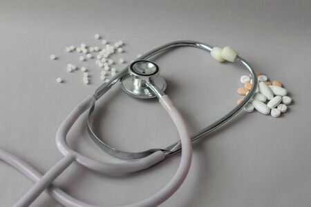 stethoscope between conventional medicines white and orange pills and natural medicines, homeopathic, white balls on gray backgroundの写真素材