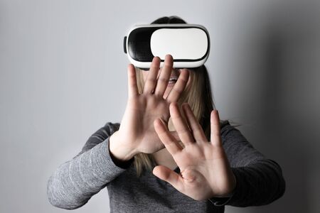 Blonde Caucasian woman wearing VR or virtual reality glasses isolated on gray background.