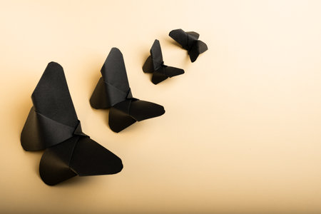 Paper butterflies, origami, black butterflies are directed towards the light or clarity. Isolated on a light gold background.の写真素材