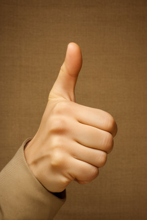 Hand with thumb up on a brown background. Close-up.の素材