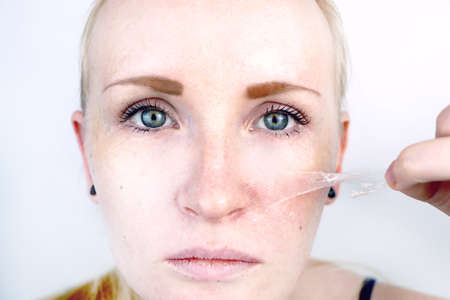 The girl removes the mask film from the face. The concept of removing old dry skin, self-careの写真素材