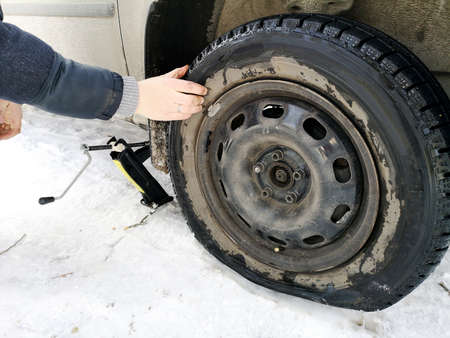 Punched and flat tire on the road. Replacing the wheel with a jack by the driverの写真素材