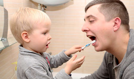 Dad and son brush their teeth in the bathroom. Father Brushing Teeth to Childの写真素材