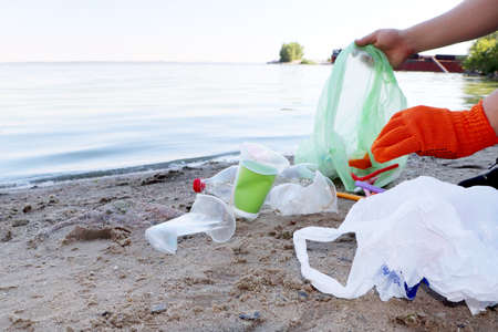 Garbage collection on the beach. Plastic and packages scattered on the beach. A man collects...