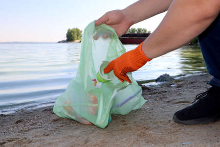 Garbage collection on the beach. Plastic and packages scattered on the beach. A man collects...