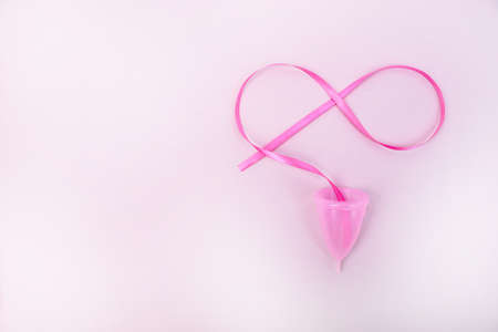 A woman holds a menstrual cup in her hand on a pink background. The concept of women's health,...