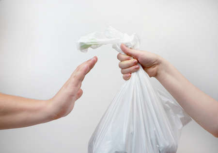 Refusal of a plastic bag. Environmental protection concept. An offer in a store to buy goods in a package, a man refuses with a stop gesture. Isolated on white background, place for an inscriptionの写真素材