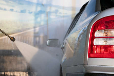 Car wash. A man washes a car under the pressure of water and rubs the glass. Car care conceptの写真素材