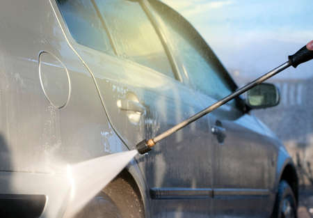 Car wash. A man washes a car under the pressure of water and rubs the glass. Car care conceptの写真素材