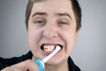A man brushes his teeth with an electric brush while looking at the camera, as if looking in a mirror. Hygiene of the oral cavityの写真素材