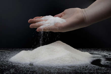 Sugar in hand on a black background. The concept of addiction to sweets. Macro photo of granulated...